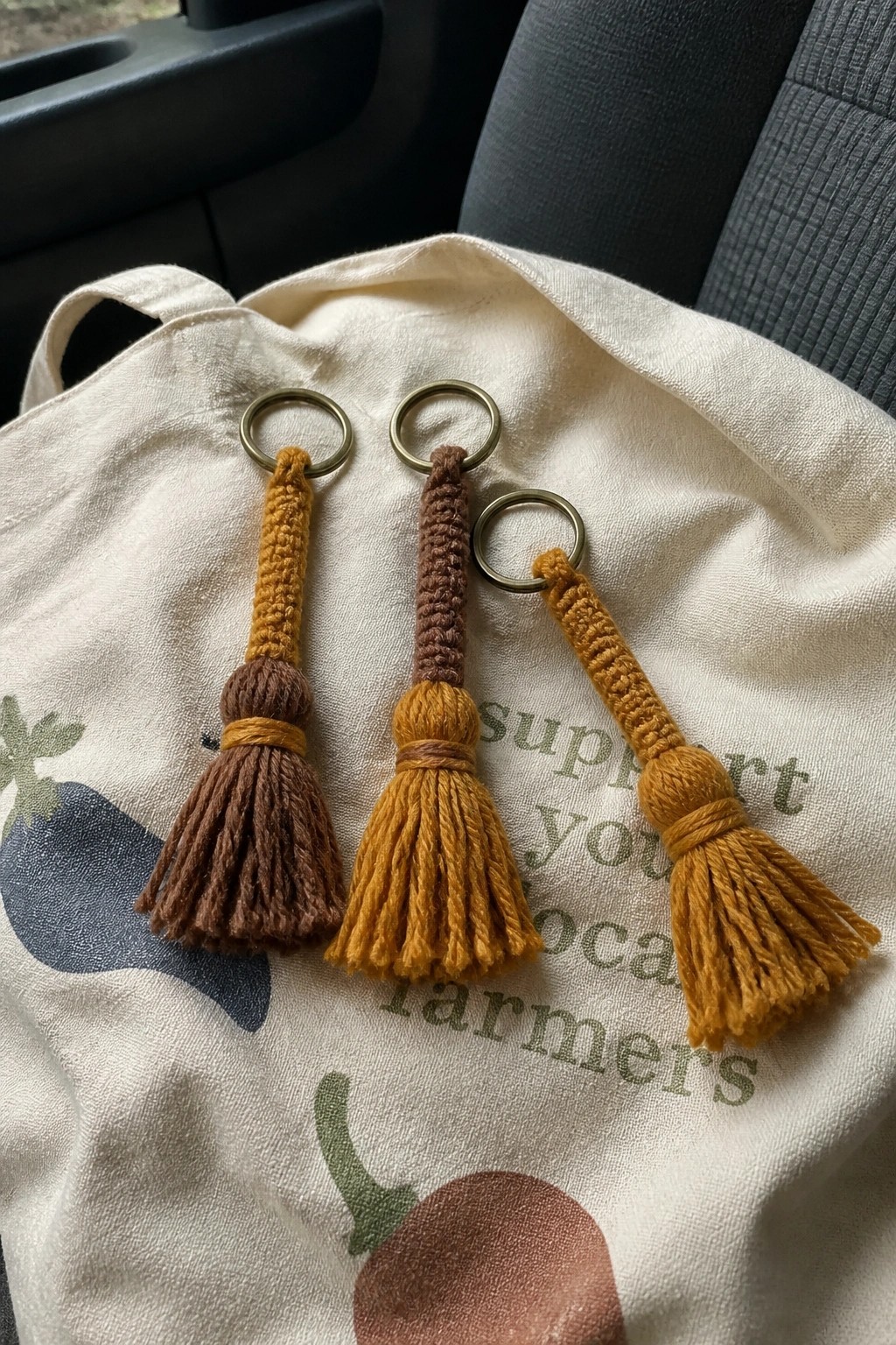 Three mustard yellow and brown tassel keychains on vegetable-print tote bag