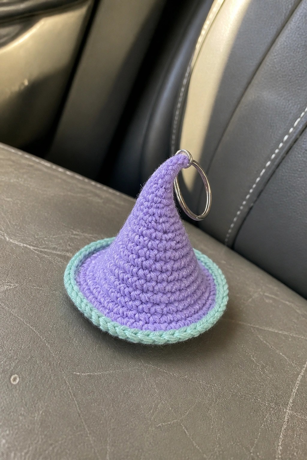 Crocheted purple witch hat keychain with mint brim on gray car seat