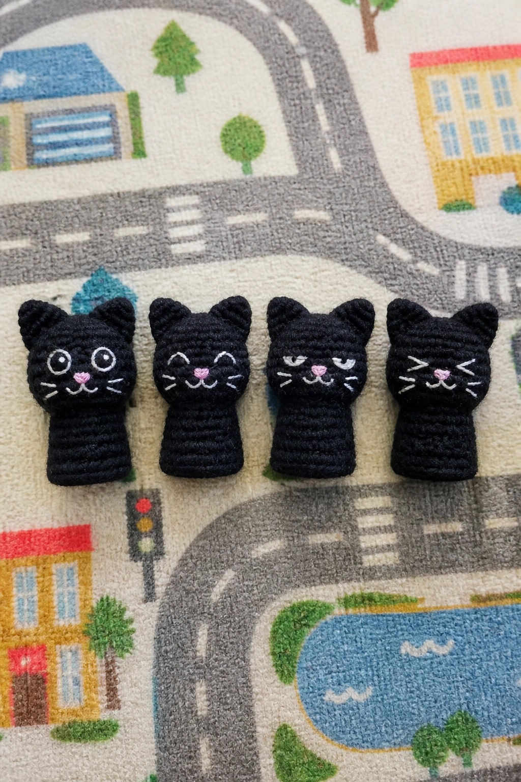 Four black crocheted cat puppets with varied embroidered expressions on a play mat.