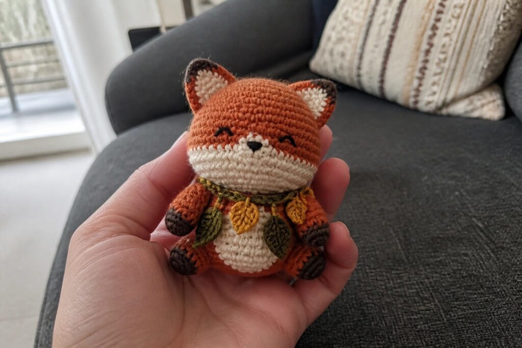 A small crocheted orange fox wearing a leaf garland held in a hand.