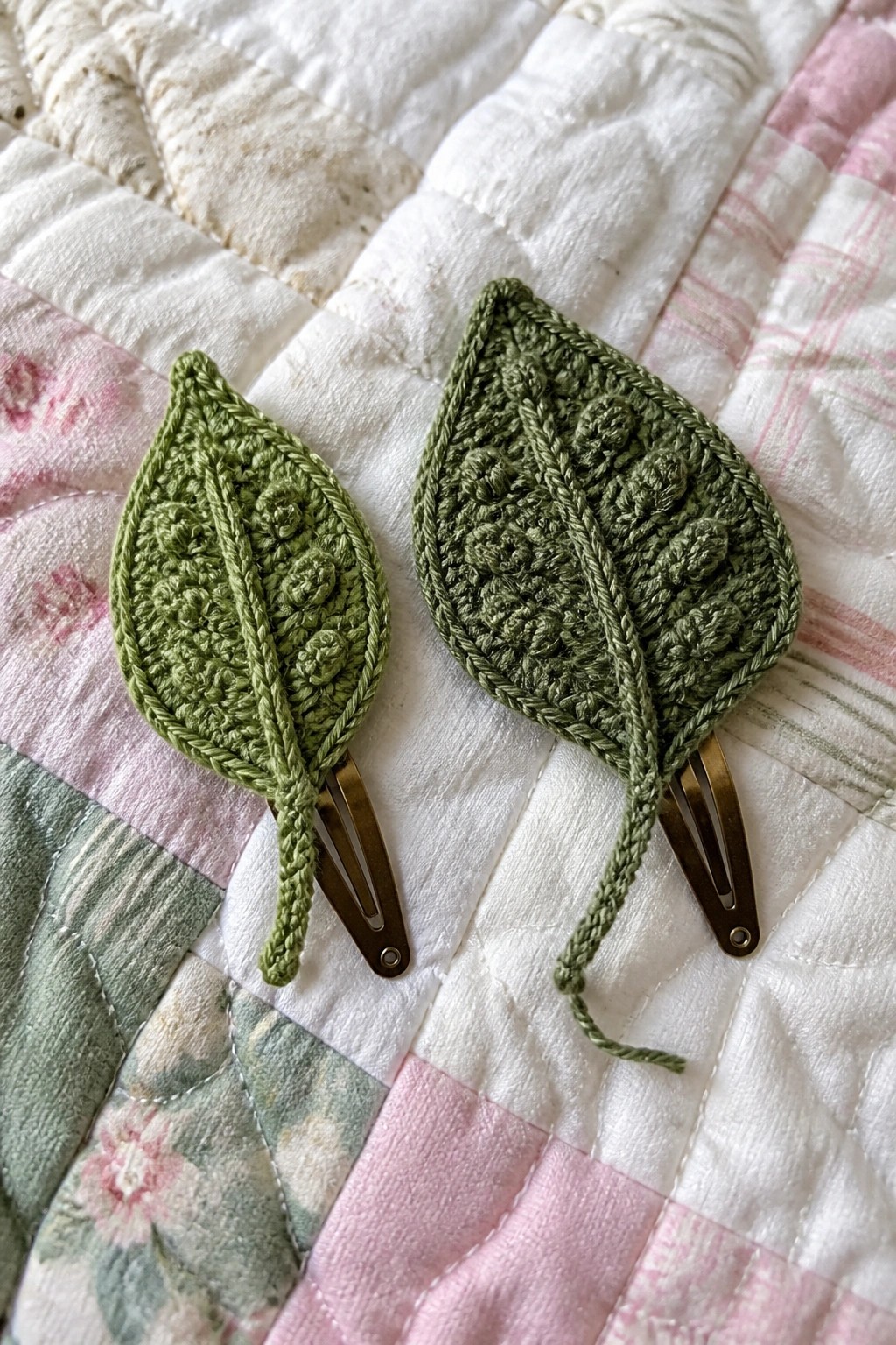 Two crocheted green leaf hair clips on a floral patchwork quilt.