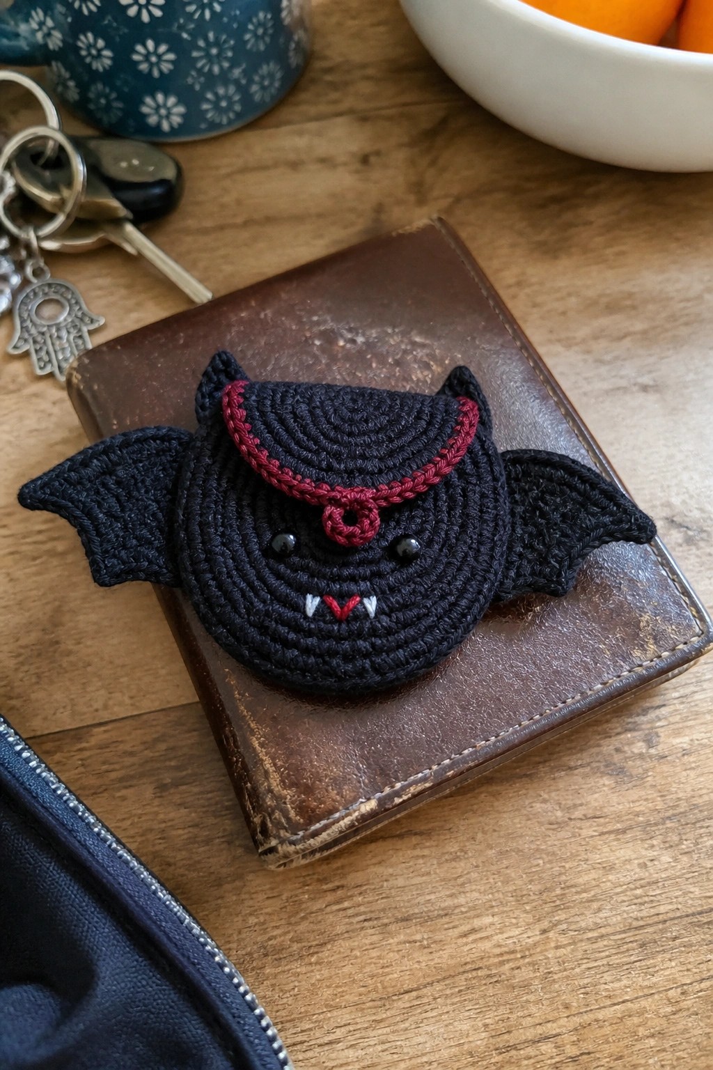 Black crocheted bat with red collar and fangs on brown leather wallet.