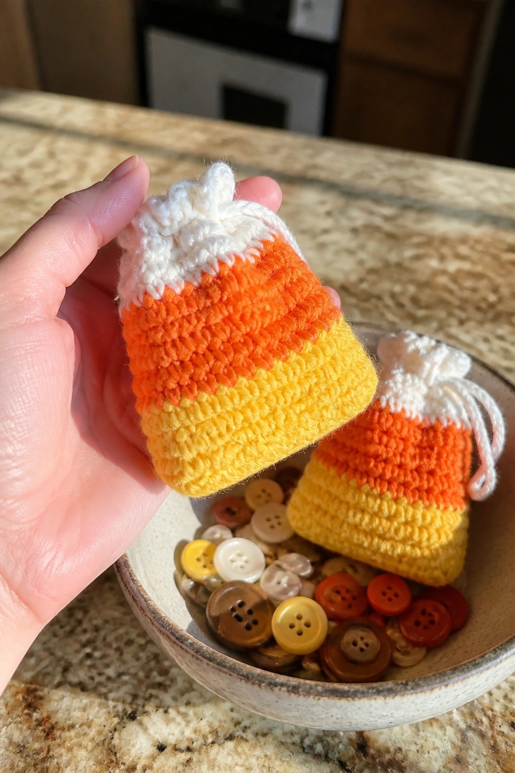 Hand holding crocheted candy corn pouch above bowl filled with buttons