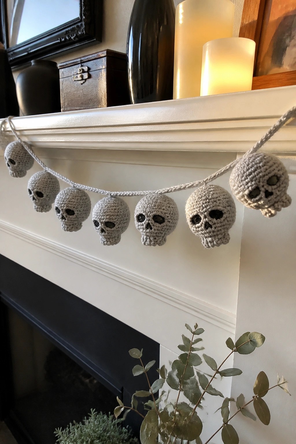 Crocheted gray skull garland draped on white fireplace mantel with candles