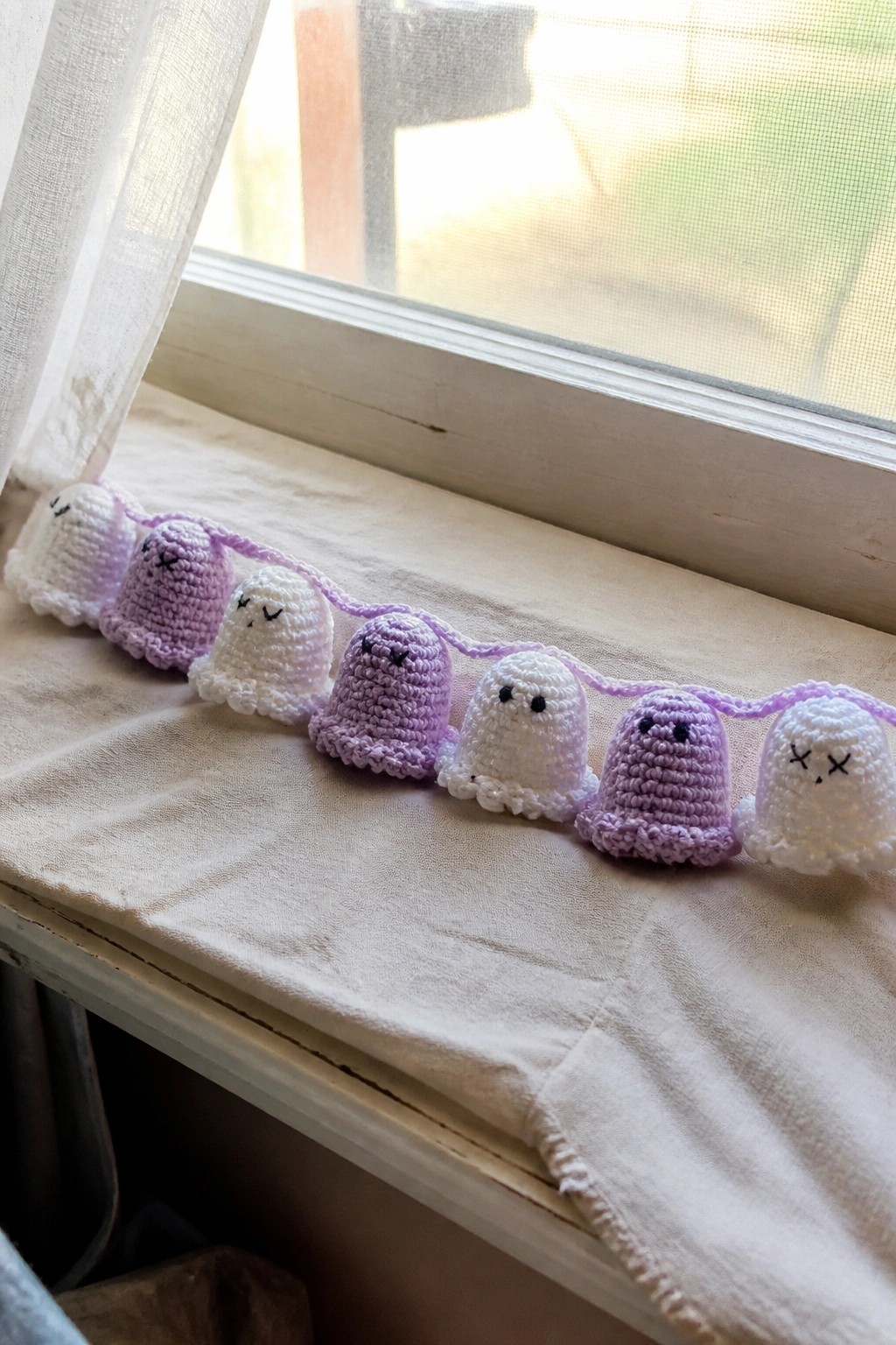 Crocheted ghost garland in white and purple yarn laid on a windowsill.