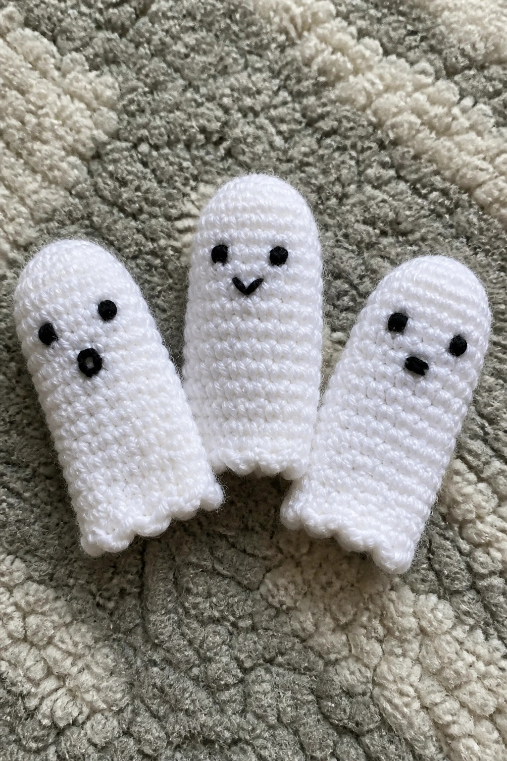 Three small white crocheted ghosts with black eyes on textured fabric