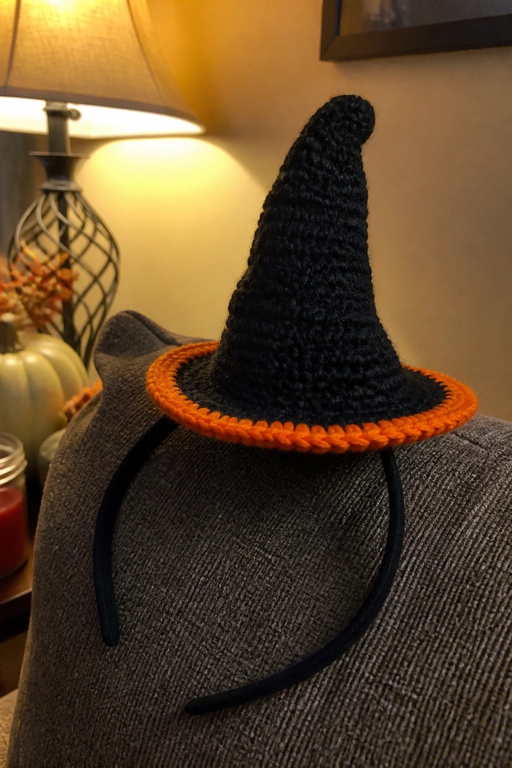 Black crocheted witch hat with orange brim on black headband over gray fabric