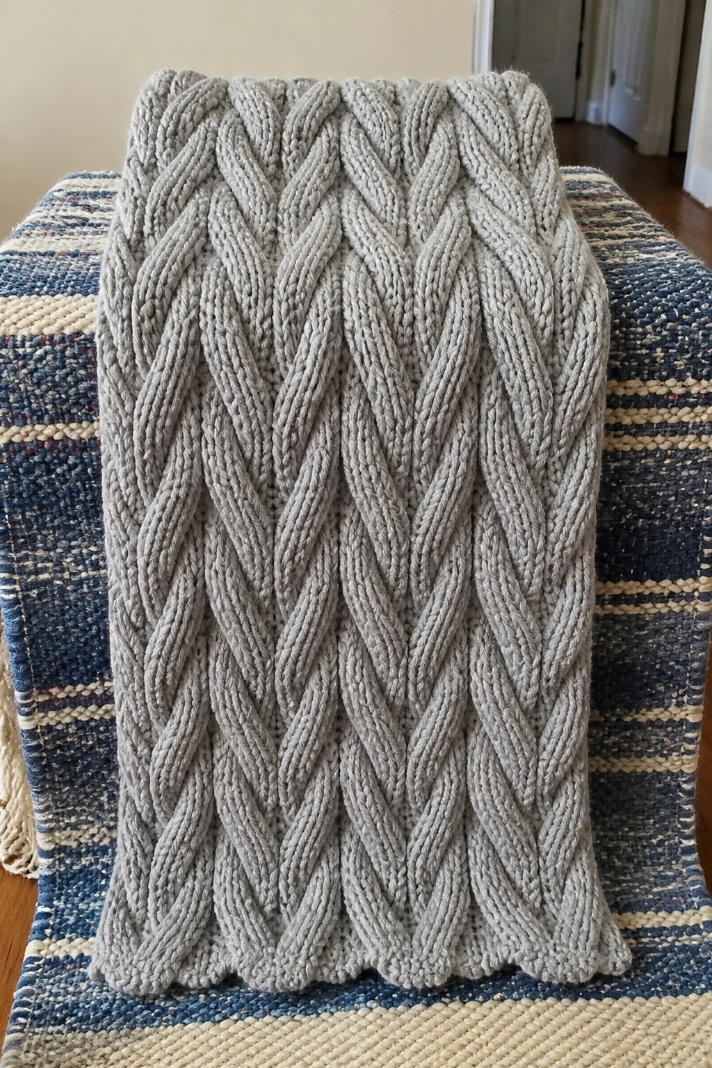 Gray cable-knit blanket with braided patterns on striped woven fabric