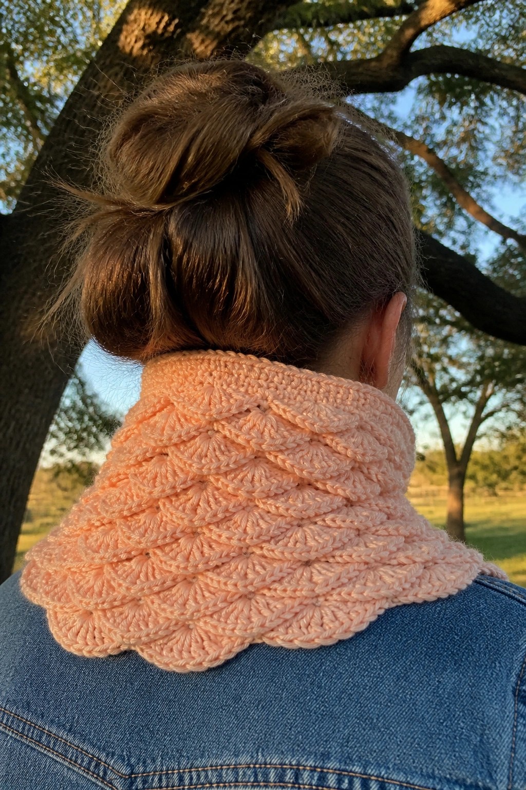 Woman with brown bun hair wearing peach crocheted cowl and blue denim jacket outdoors