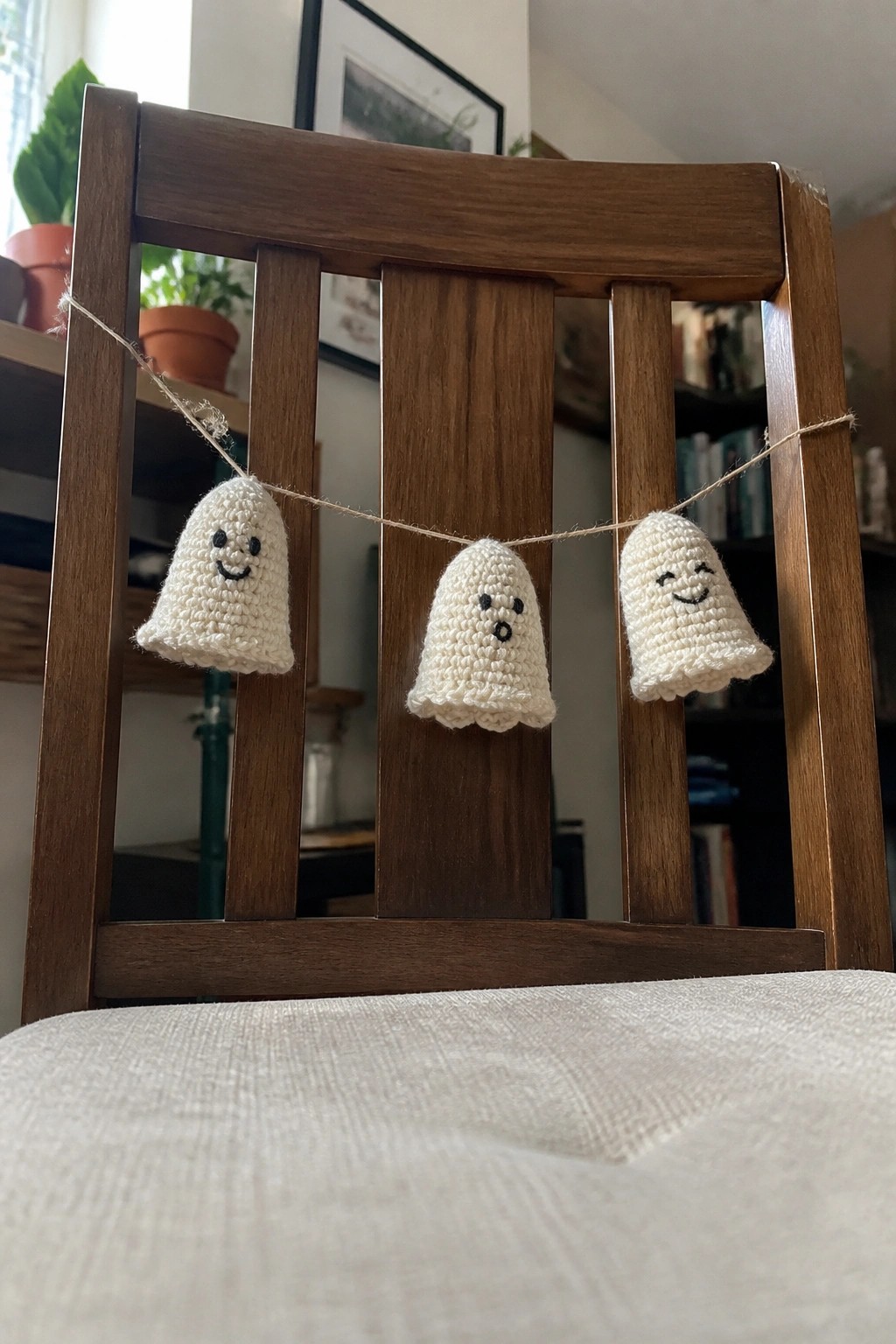 Three crocheted white ghosts with faces strung across wooden chair back