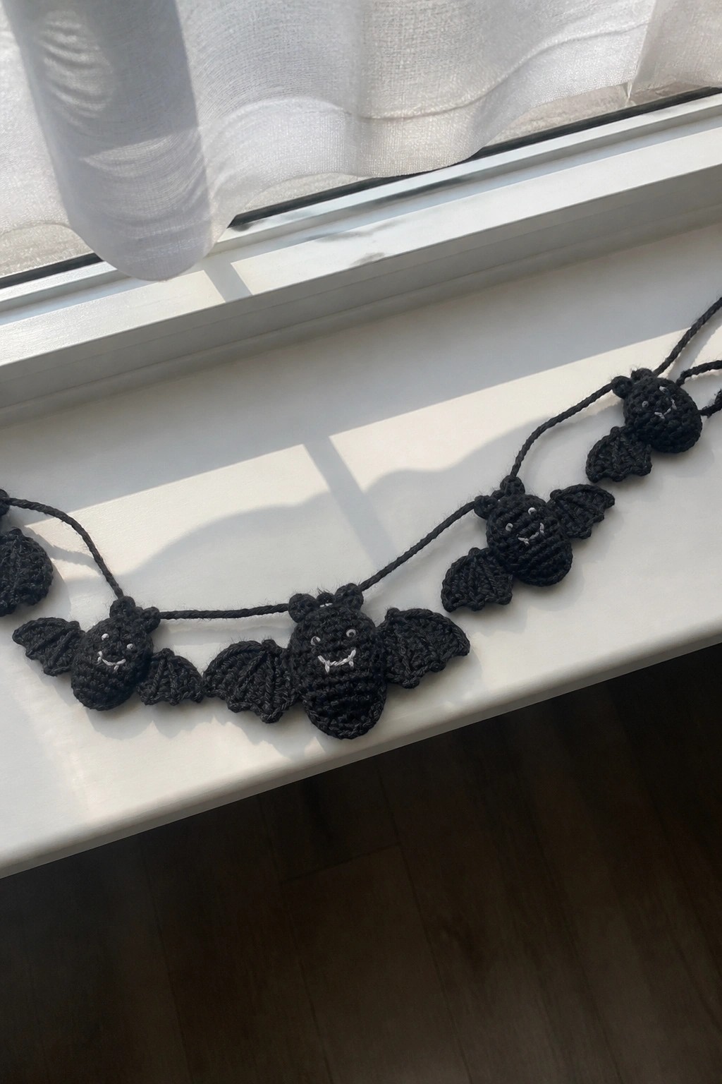 Black crocheted bats with faces strung across a white windowsill.