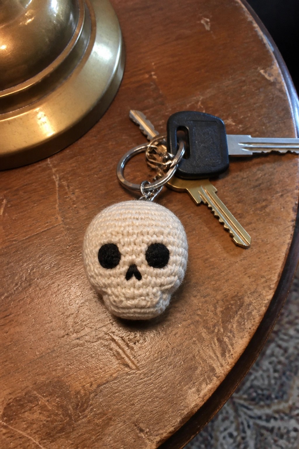 Crocheted white skull keychain with black eyes beside keys on wooden table