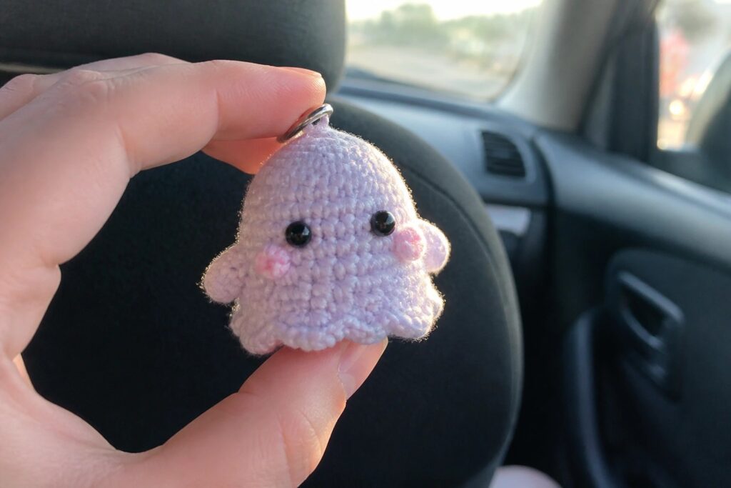 Hand holding small purple crocheted octopus keychain with black eyes in car.