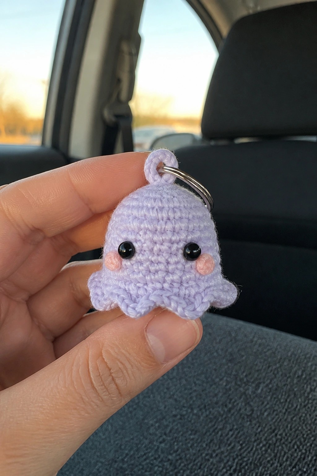 Hand holding small purple crocheted octopus keychain with black eyes in car.