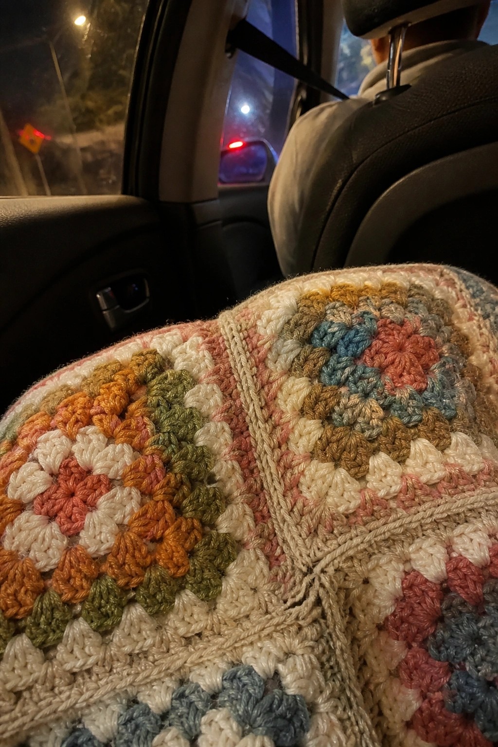 Colorful crocheted granny square blanket on a car backseat at night.