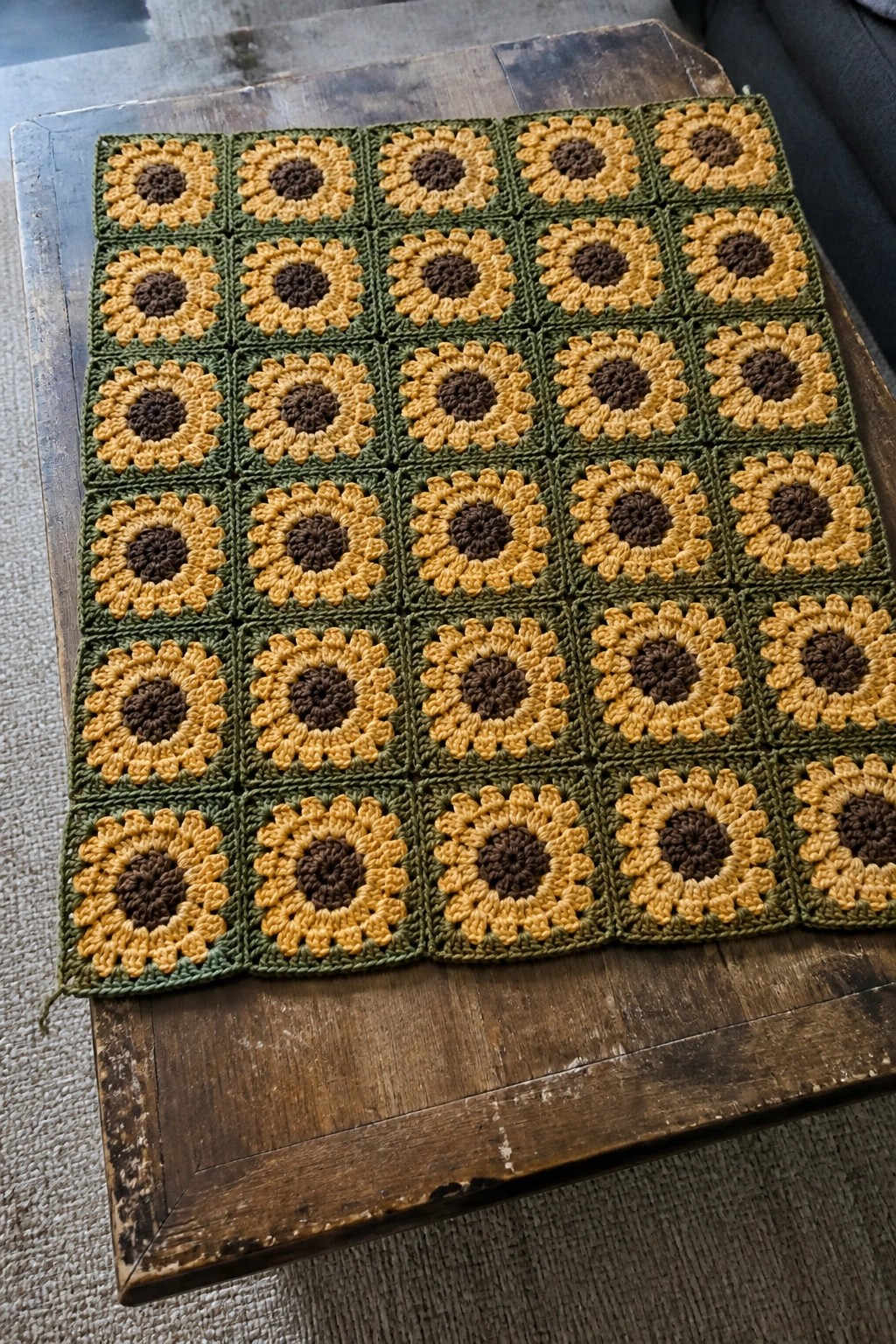 Crocheted sunflower blanket in yellow, brown, and green squares on wooden table.