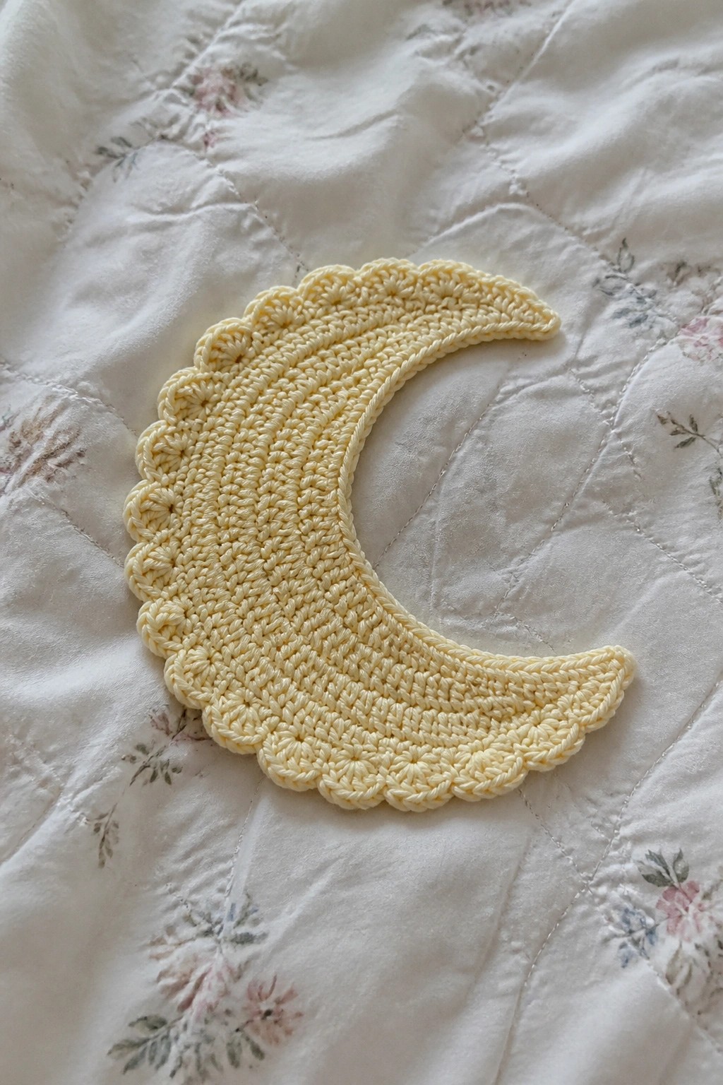 Yellow crocheted crescent moon with scalloped edges on floral quilt.