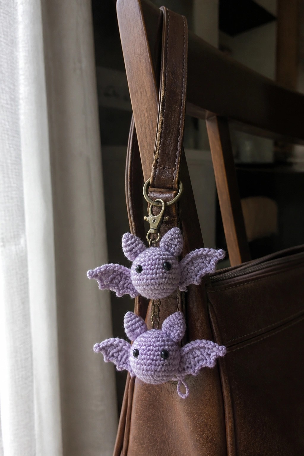 Two purple crocheted bat keychains dangling from a brown leather bag strap.