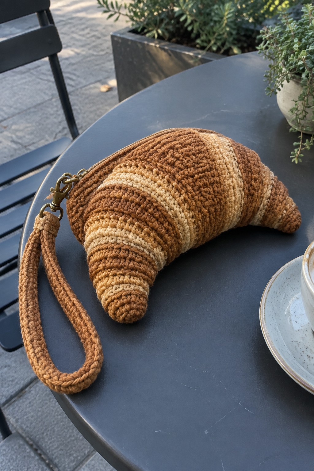 Crocheted croissant pouch in brown tones with wrist strap on dark outdoor table