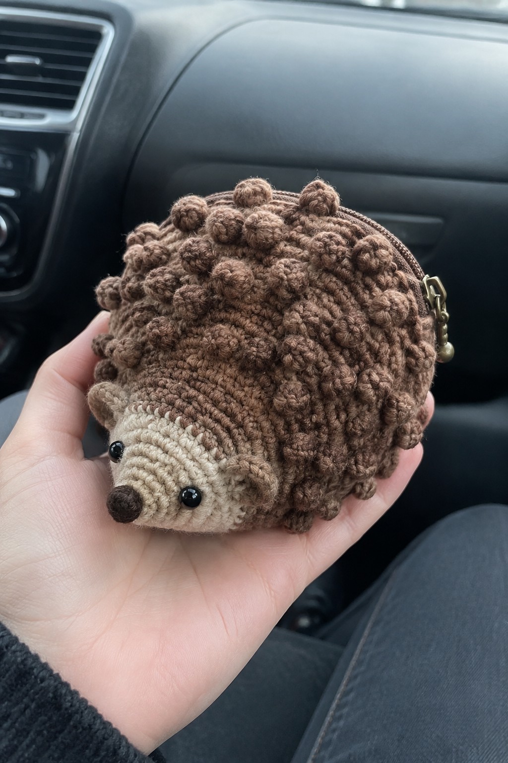 Hand holding brown crocheted hedgehog coin purse with zipper in car interior