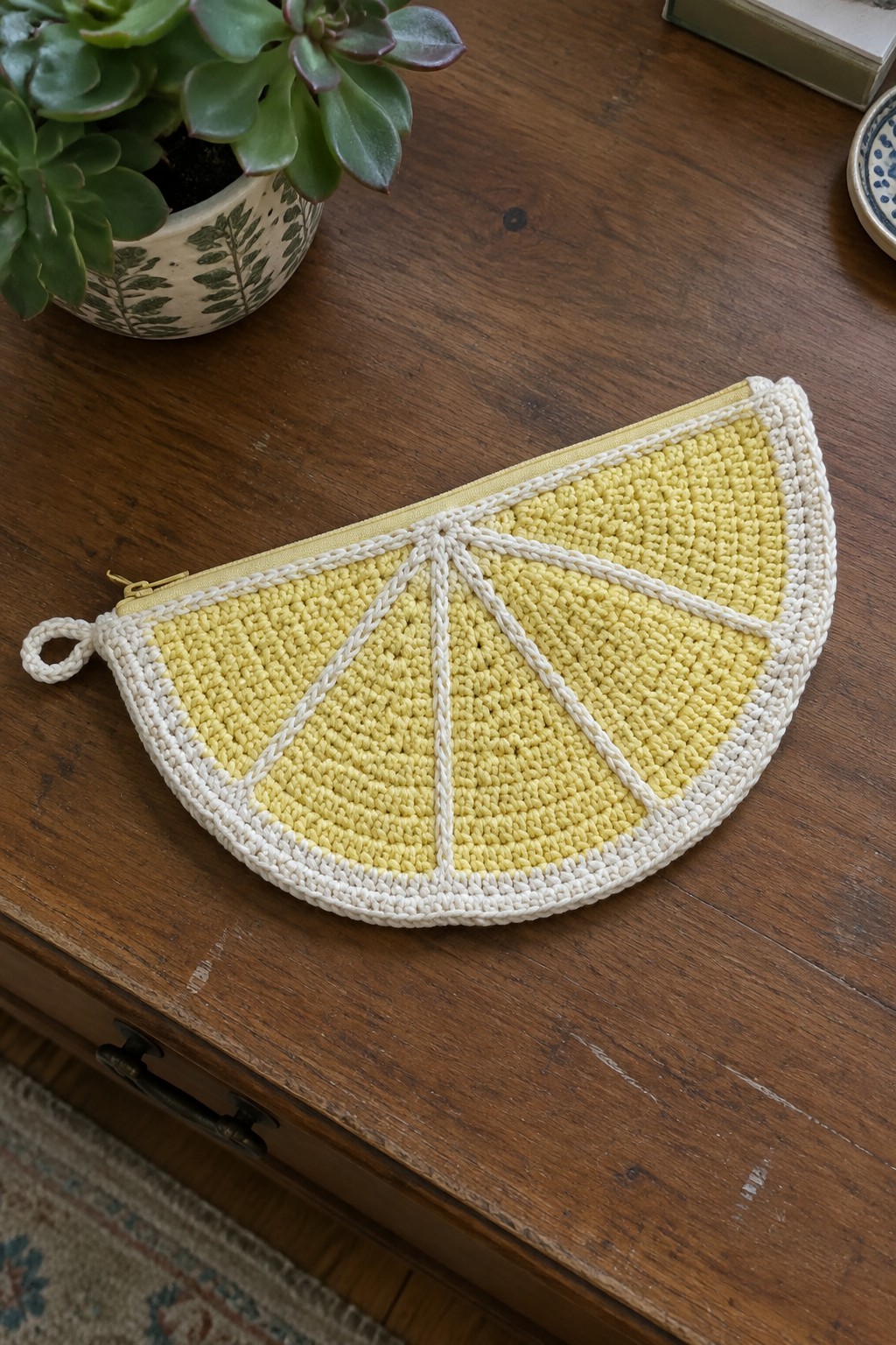 Crocheted lemon slice pouch in yellow and white yarn with a zipper along the top edge resting on a wooden table.