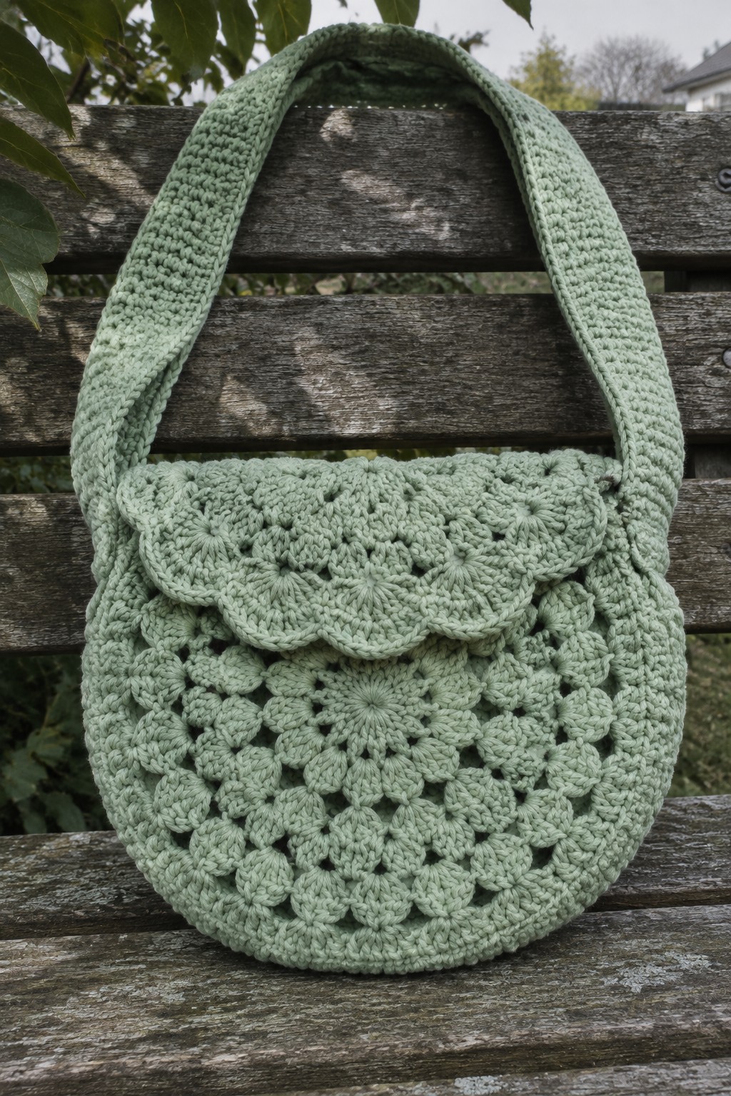 Light green crocheted handbag with scalloped flap on wooden bench