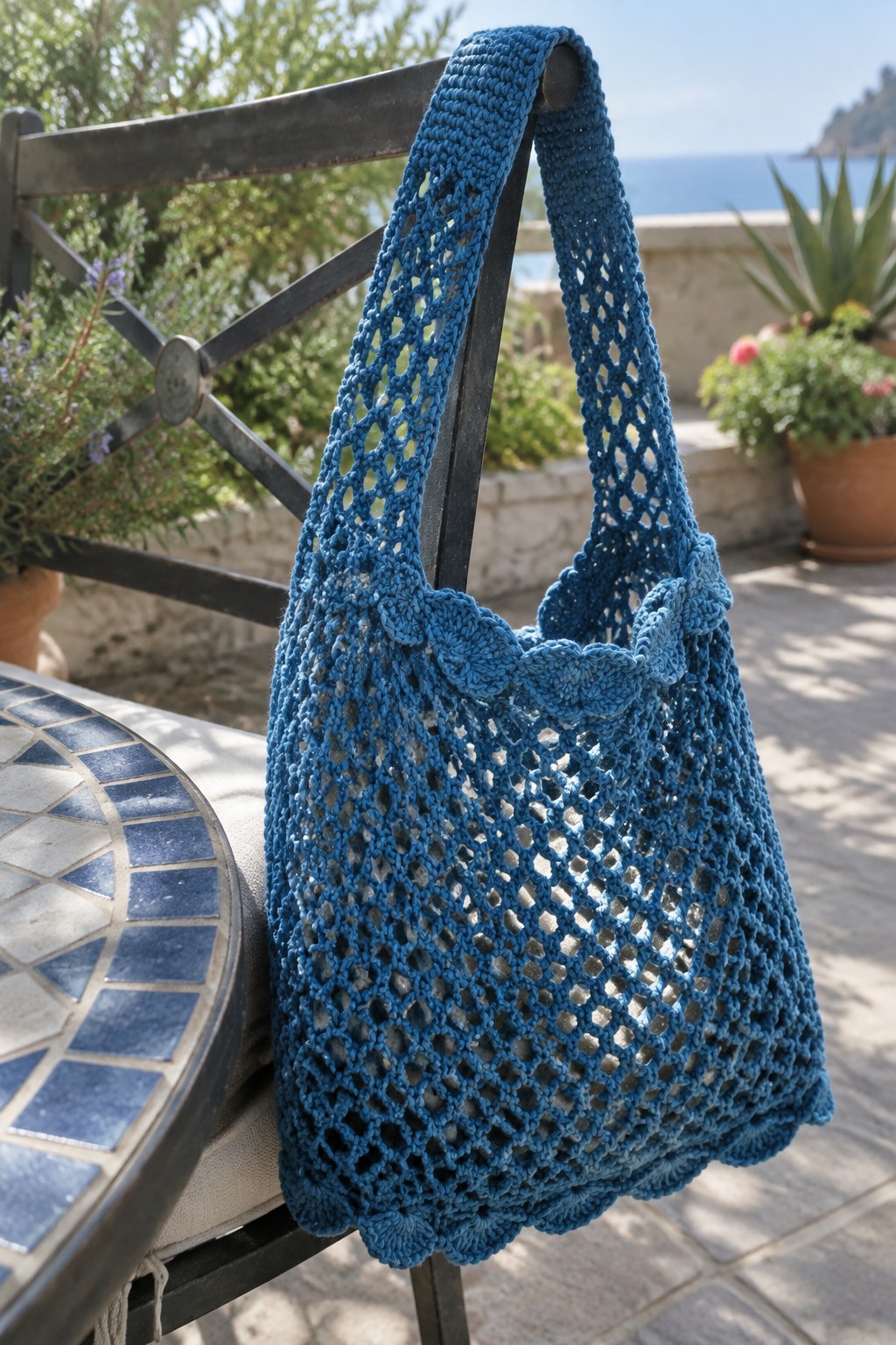 Blue crocheted mesh tote bag hanging on black metal chair by the sea