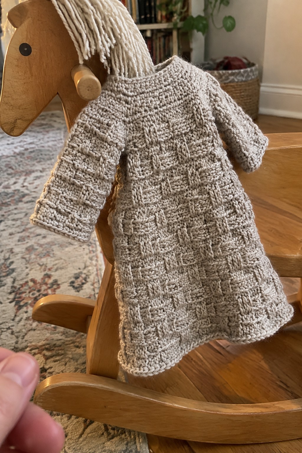 Beige cable-knit dress draped on wooden rocking horse with white yarn mane