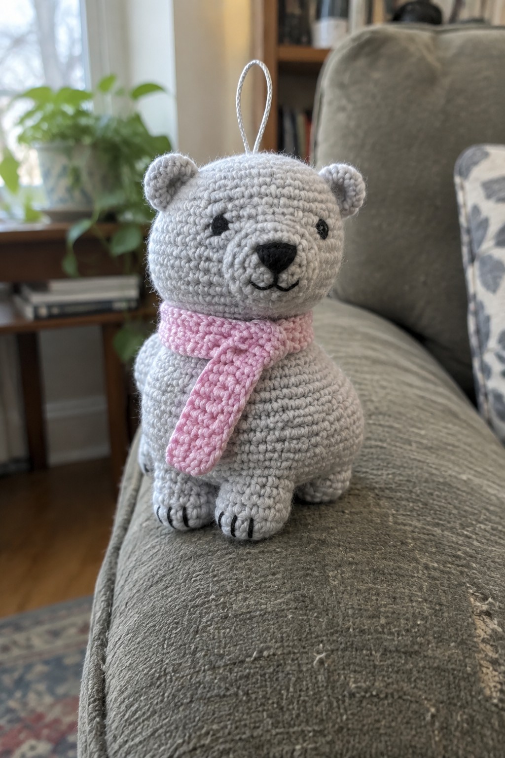 Gray crocheted polar bear with pink scarf sitting on gray couch