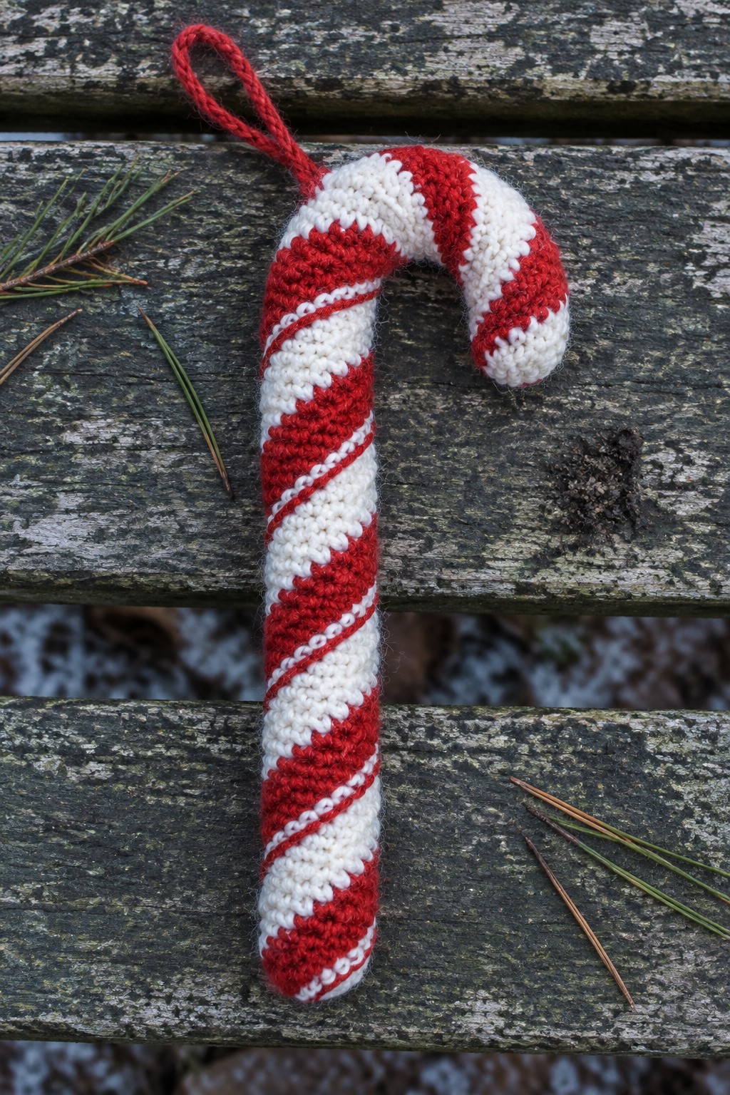 Red and white knitted candy cane ornament on weathered wooden planks with pine needles