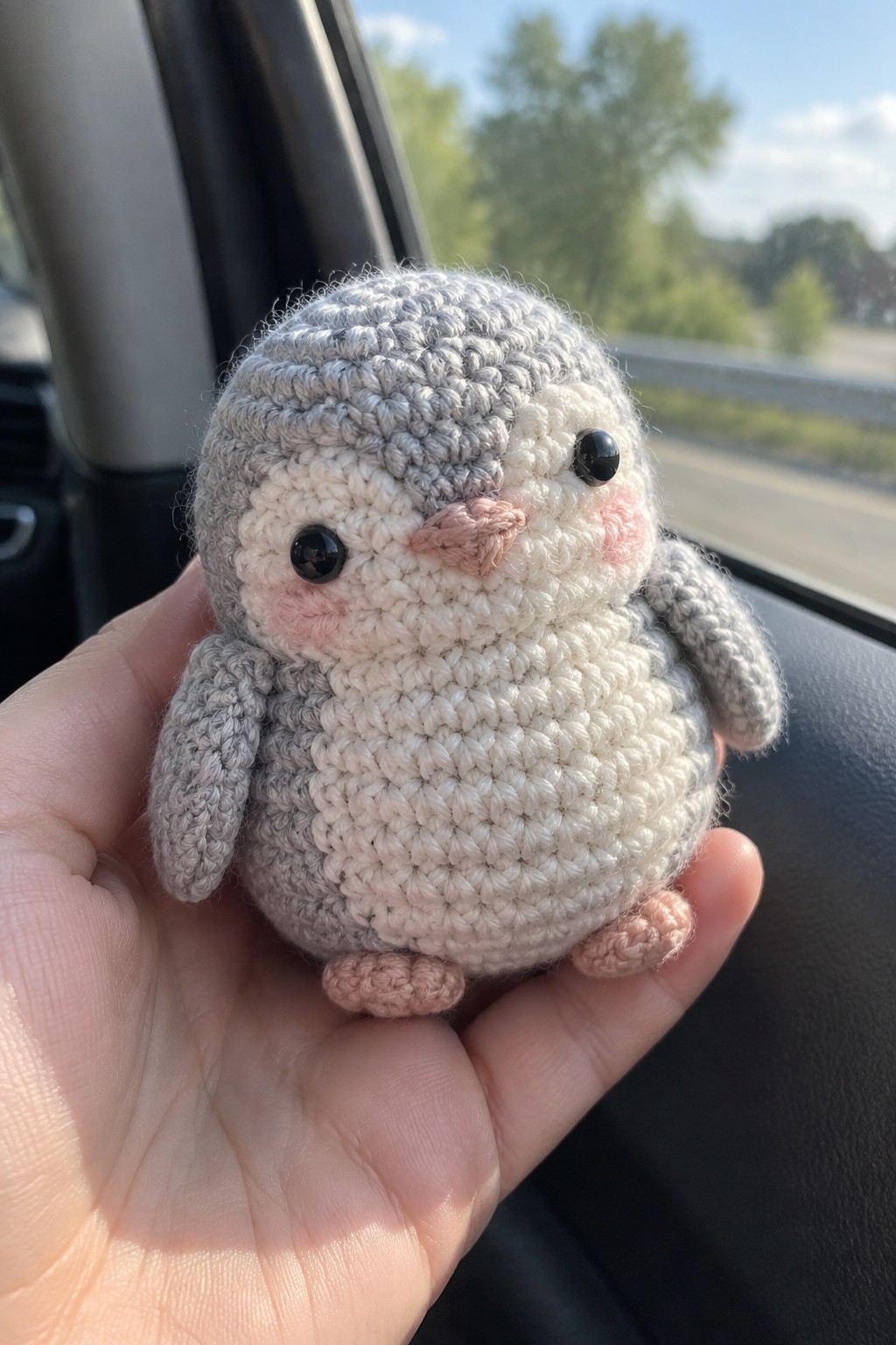 A small crocheted penguin plush toy in gray and white held in a hand.