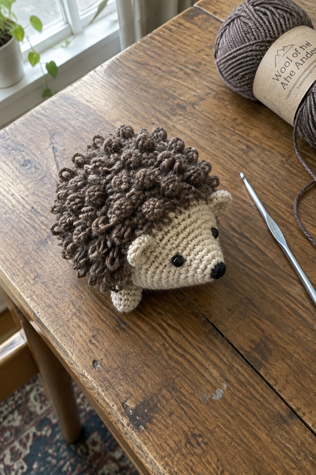 Crocheted hedgehog with brown curly spikes beside yarn ball and hook on wooden table