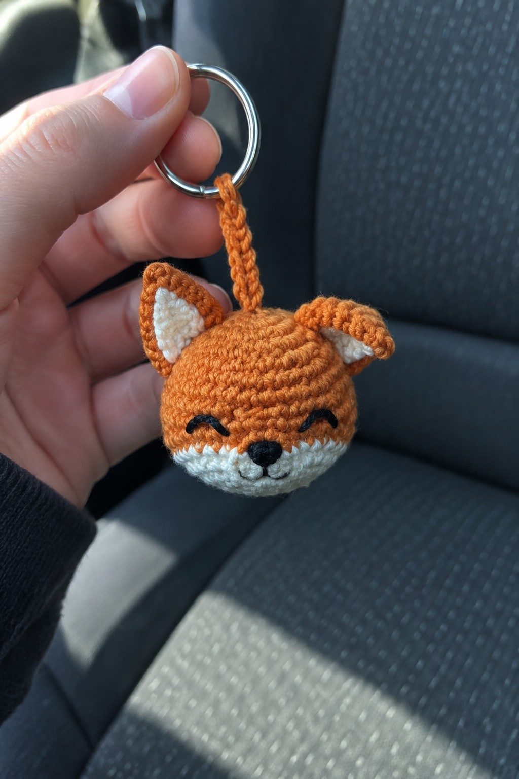 Hand holding crocheted orange fox keychain with white muzzle on metal ring