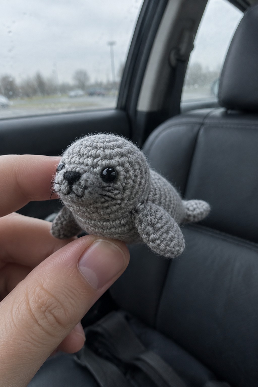 Hand holding gray crocheted seal toy inside car with black seats