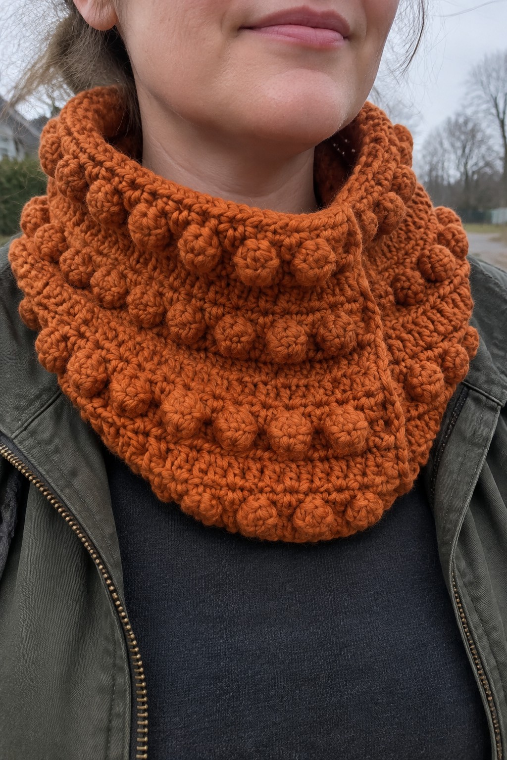 Orange bobble-knit cowl draped over a green jacket collar.
