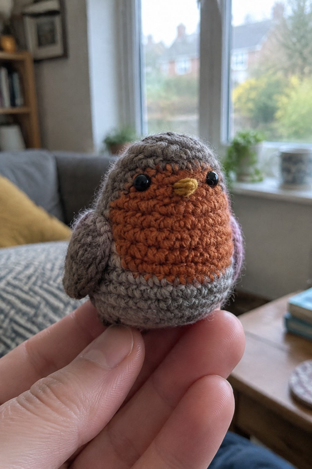 Hand holding a crocheted robin toy with gray body and orange breast.