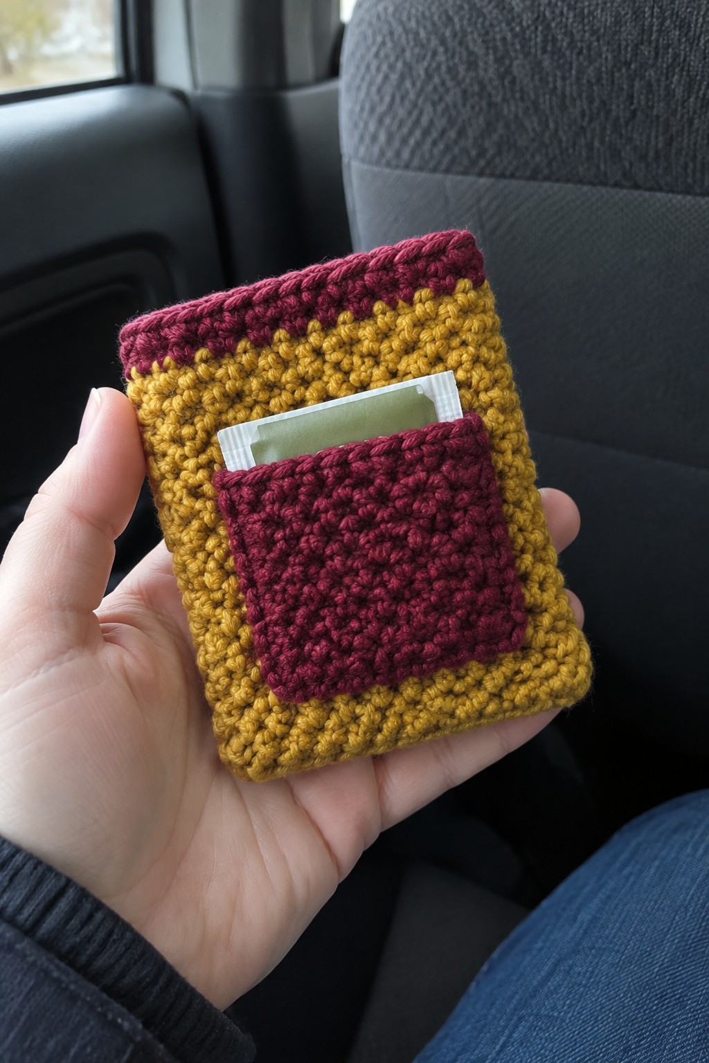 Hand holds yellow and maroon crocheted pouch with tea bag in car pocket