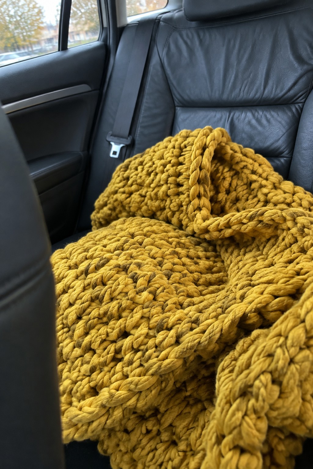 Yellow chunky knit blanket on black leather car back seat