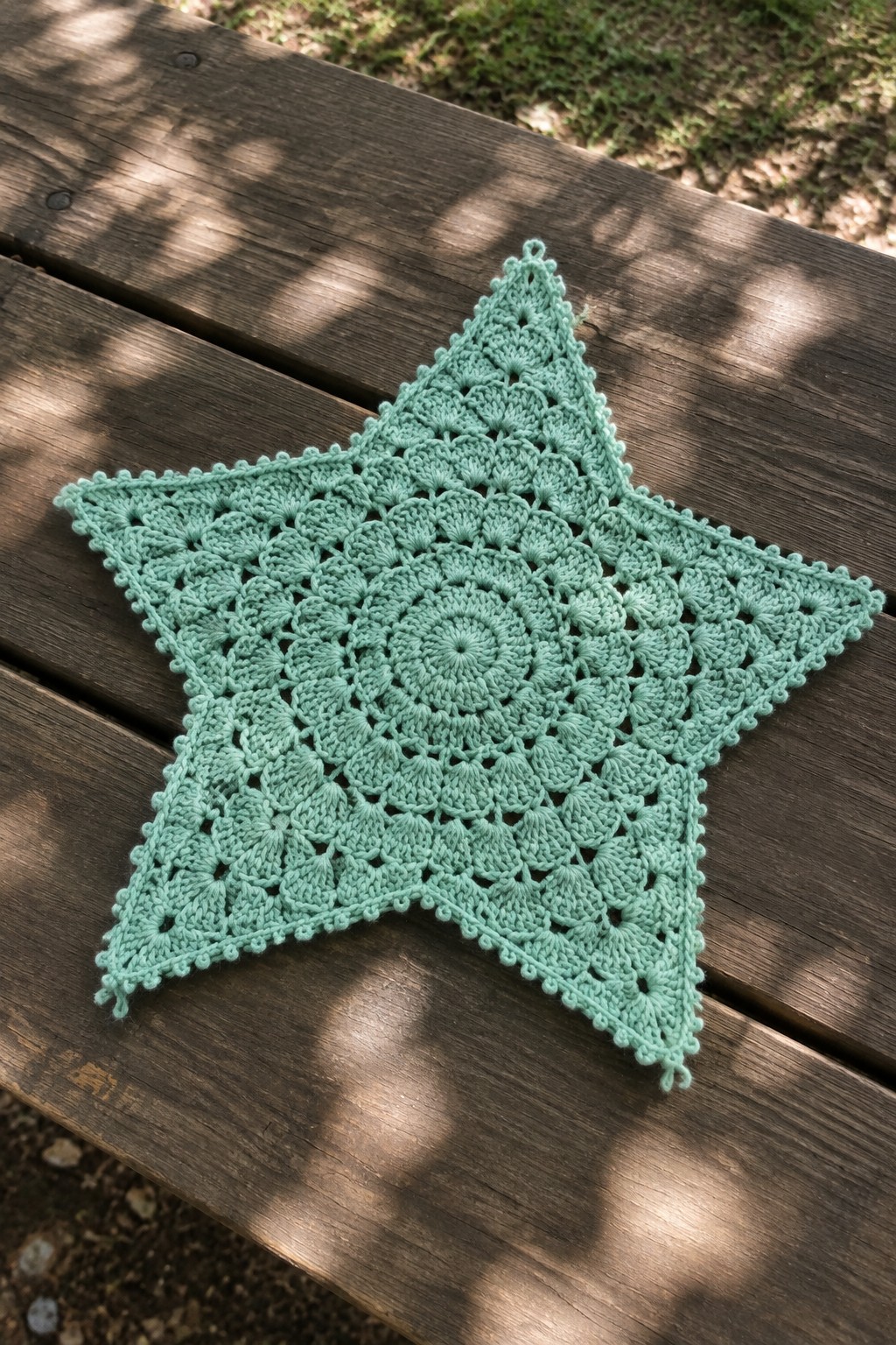 Mint green crocheted lace star on wooden picnic table in sunlight