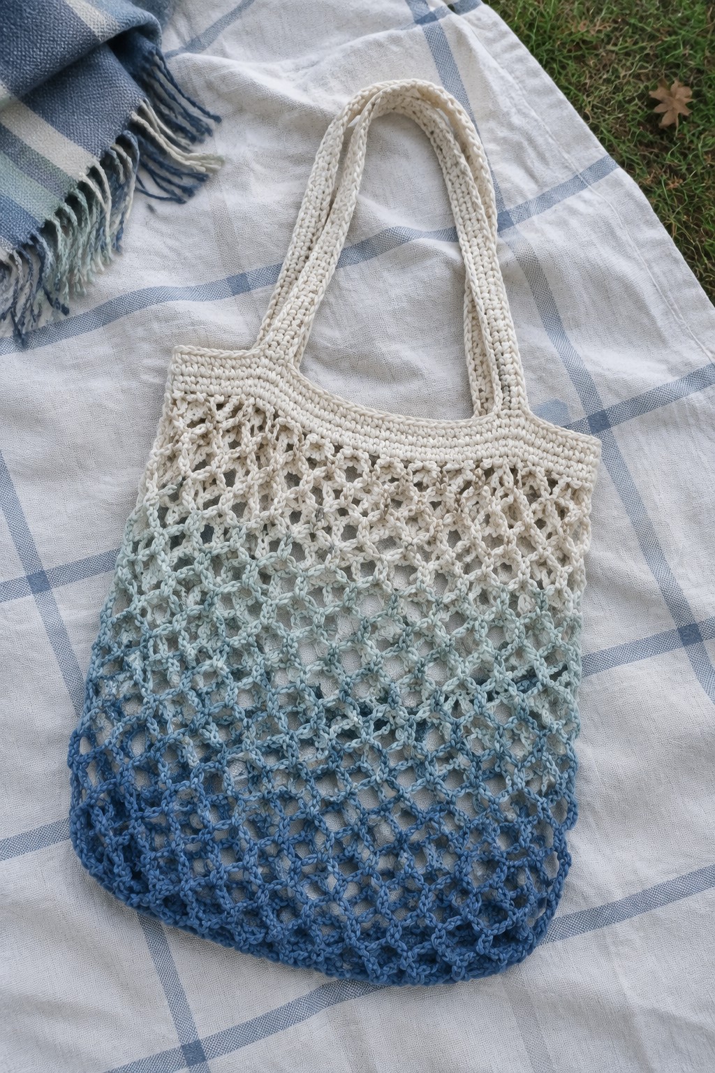 Ombre blue crocheted mesh tote bag on checkered picnic blanket outdoors