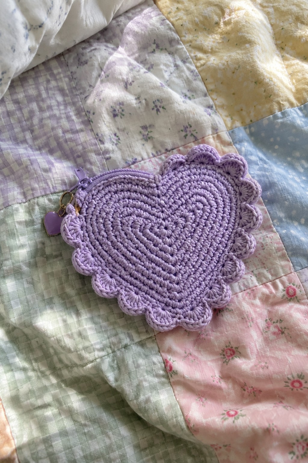 Purple crocheted heart-shaped zippered pouch with charm on patchwork quilt
