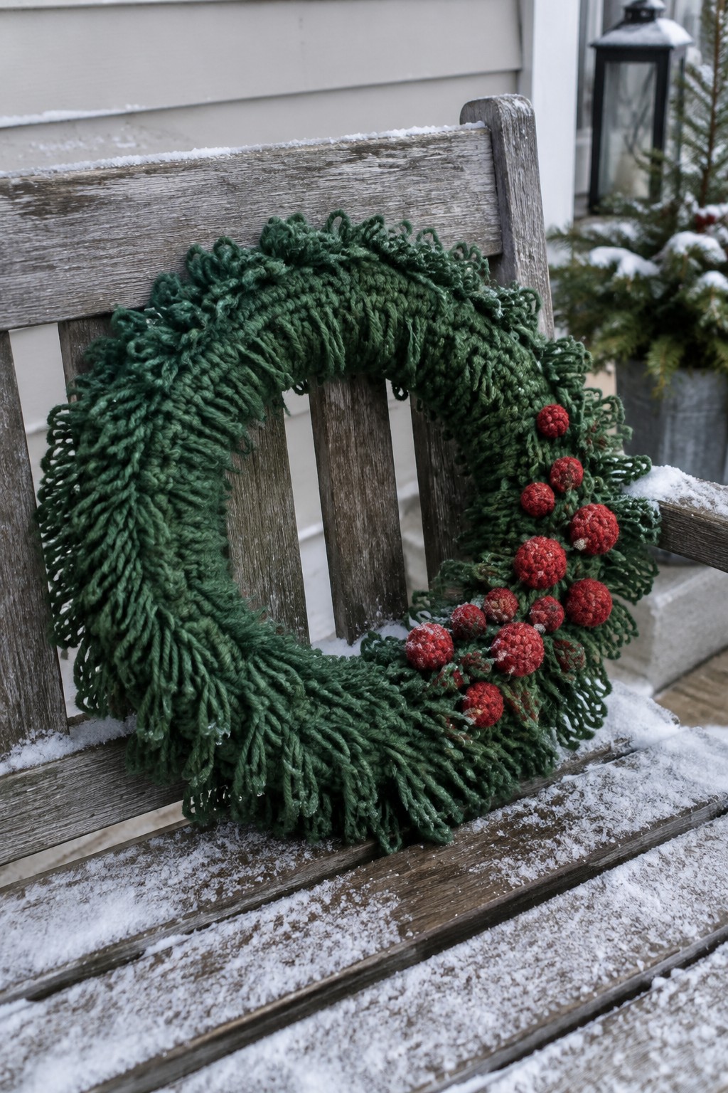 Green shaggy wreath with red berries on snow-covered wooden bench.