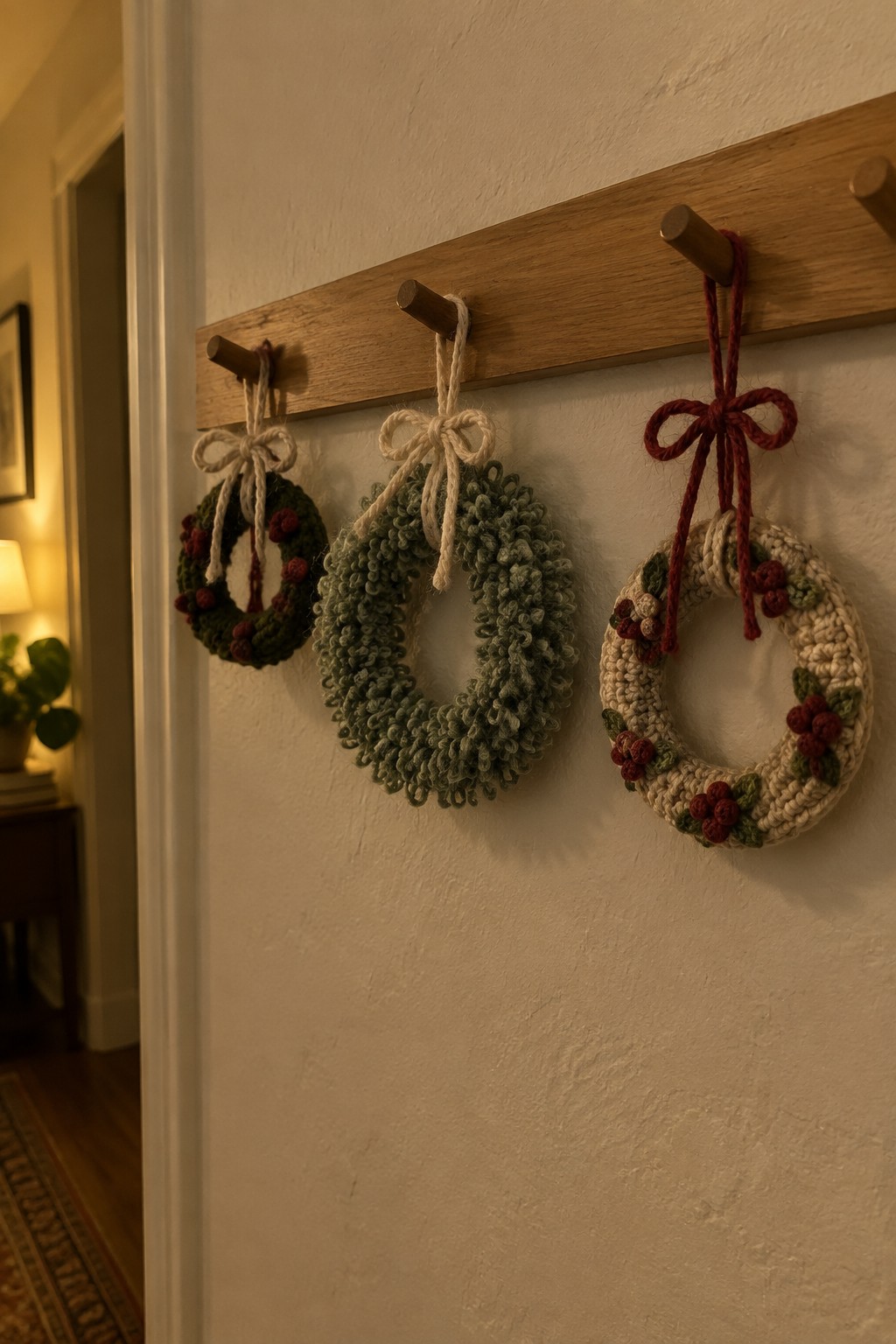 Three crocheted wreaths in green and beige hang from wooden pegs on wall