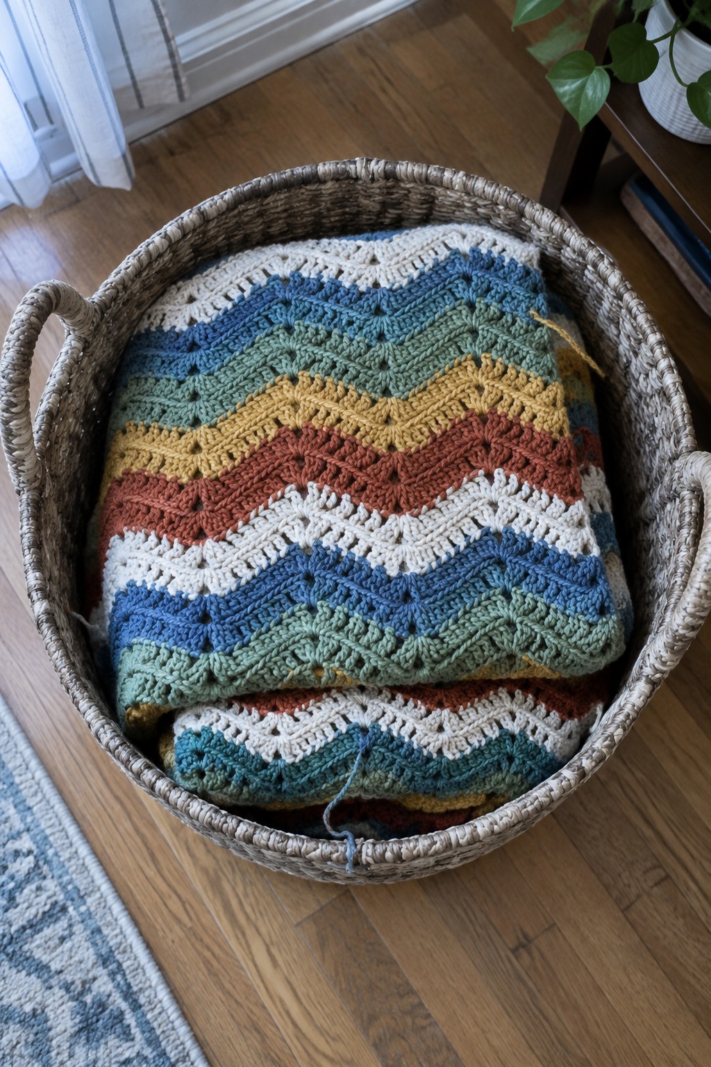 Woven basket holding folded colorful chevron crochet blanket on wooden floor.