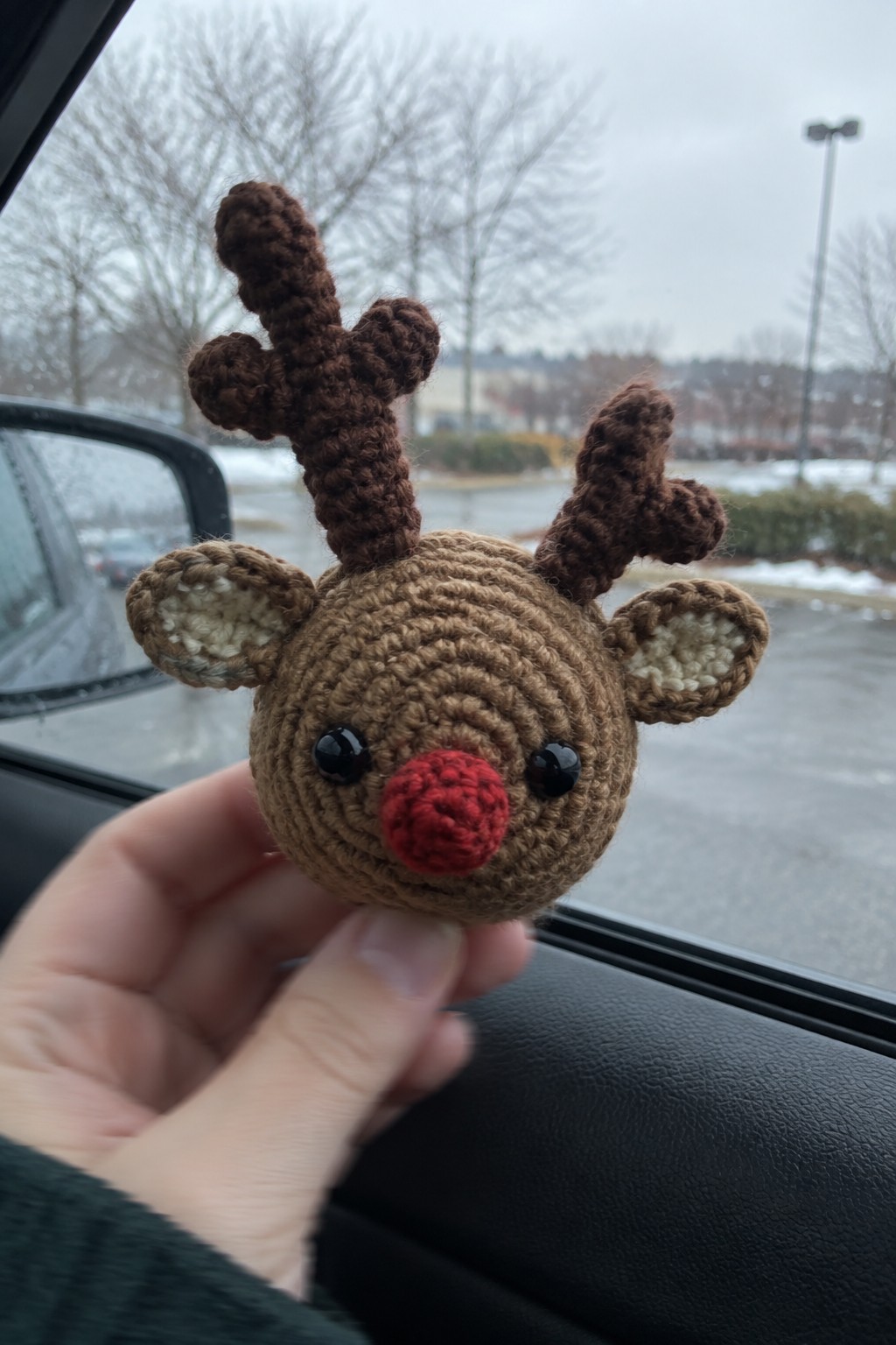 Hand holding crocheted brown reindeer with red nose, black eyes, and antlers in car.