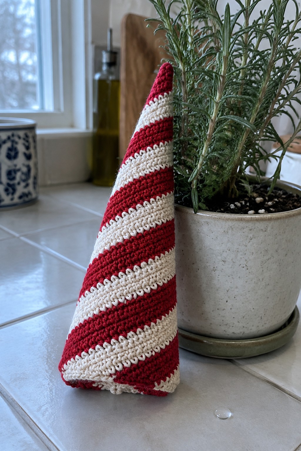 Red and white striped crocheted cone beside potted rosemary on kitchen counter