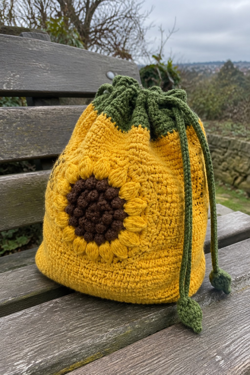 Crocheted yellow sunflower drawstring bag with brown center on wooden bench