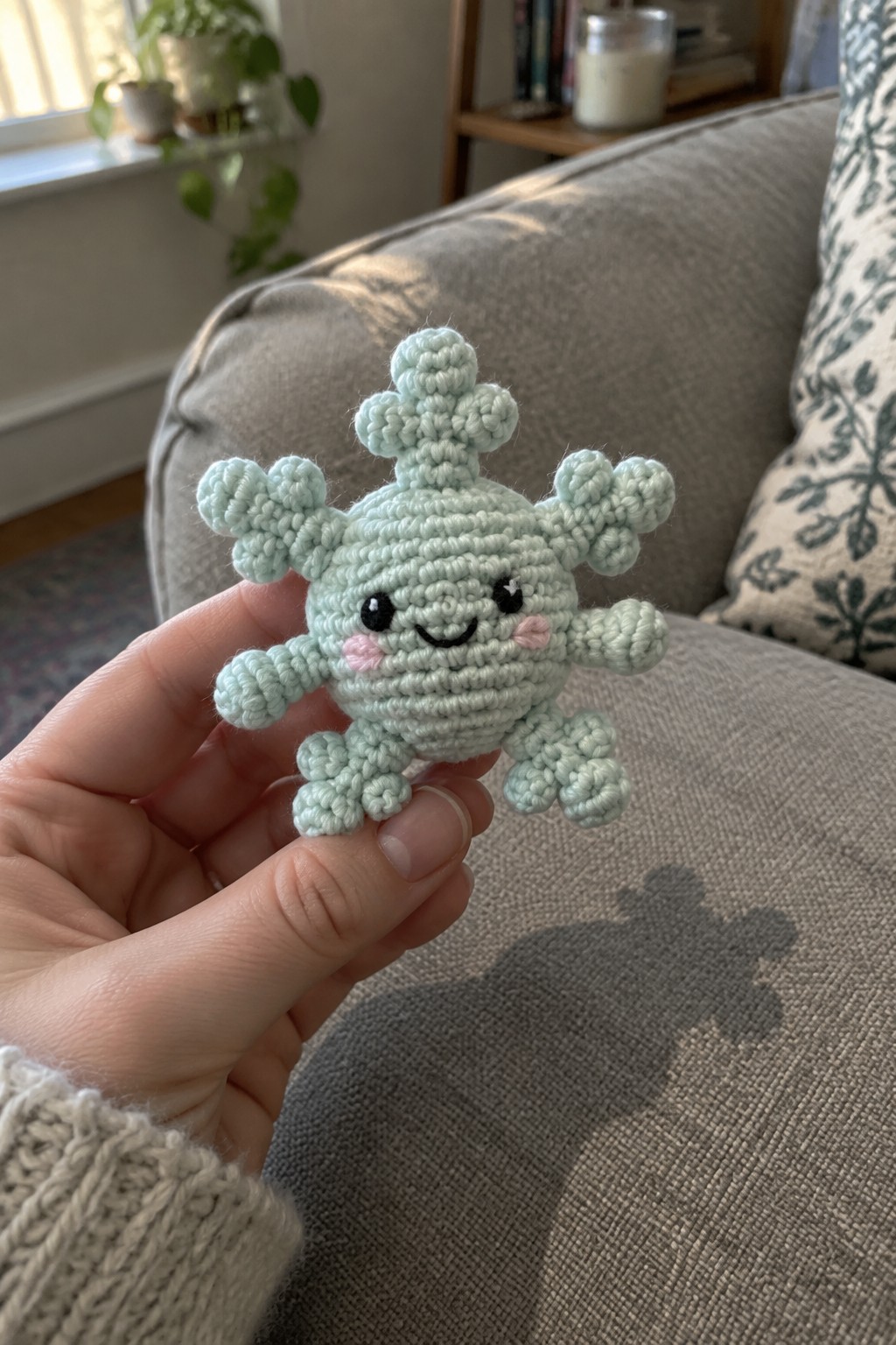 Hand holding light blue crocheted virus plush with smiling face and spikes.