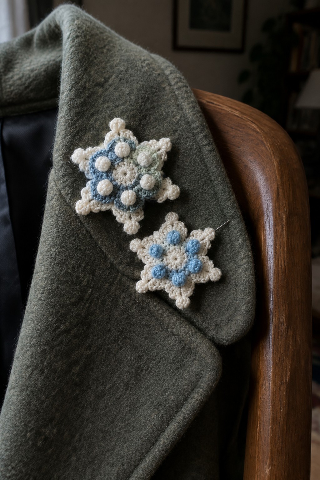 Two crocheted snowflakes pinned to a green wool coat on a wooden chair.