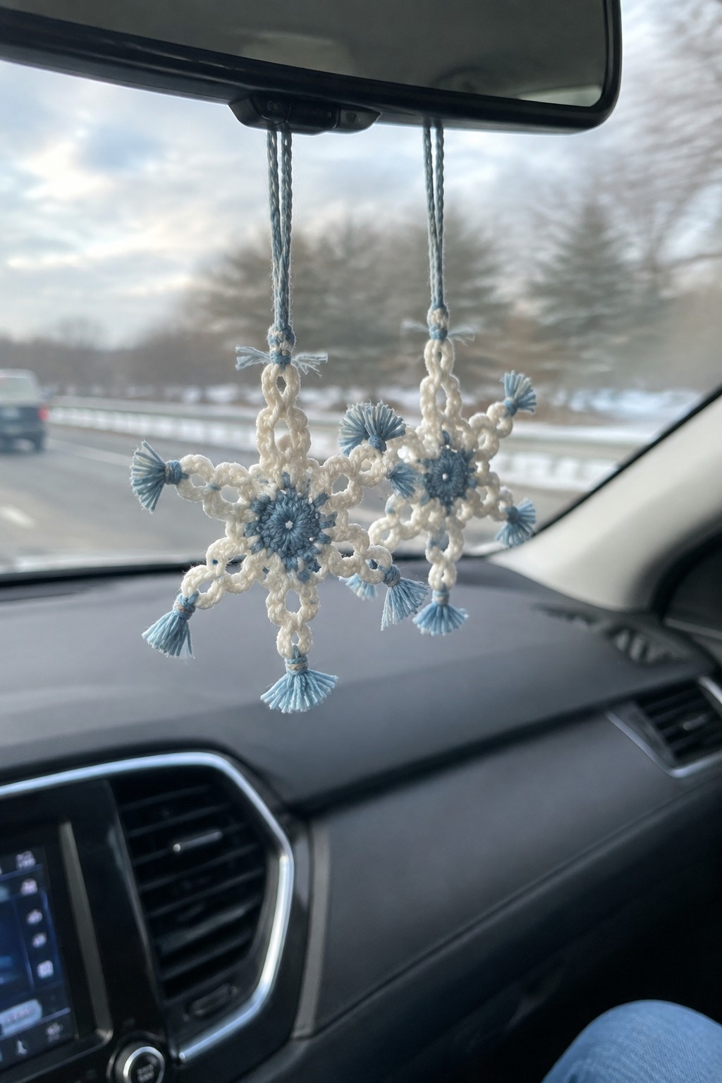 Two crocheted white snowflakes with blue accents hang from a car's rearview mirror.